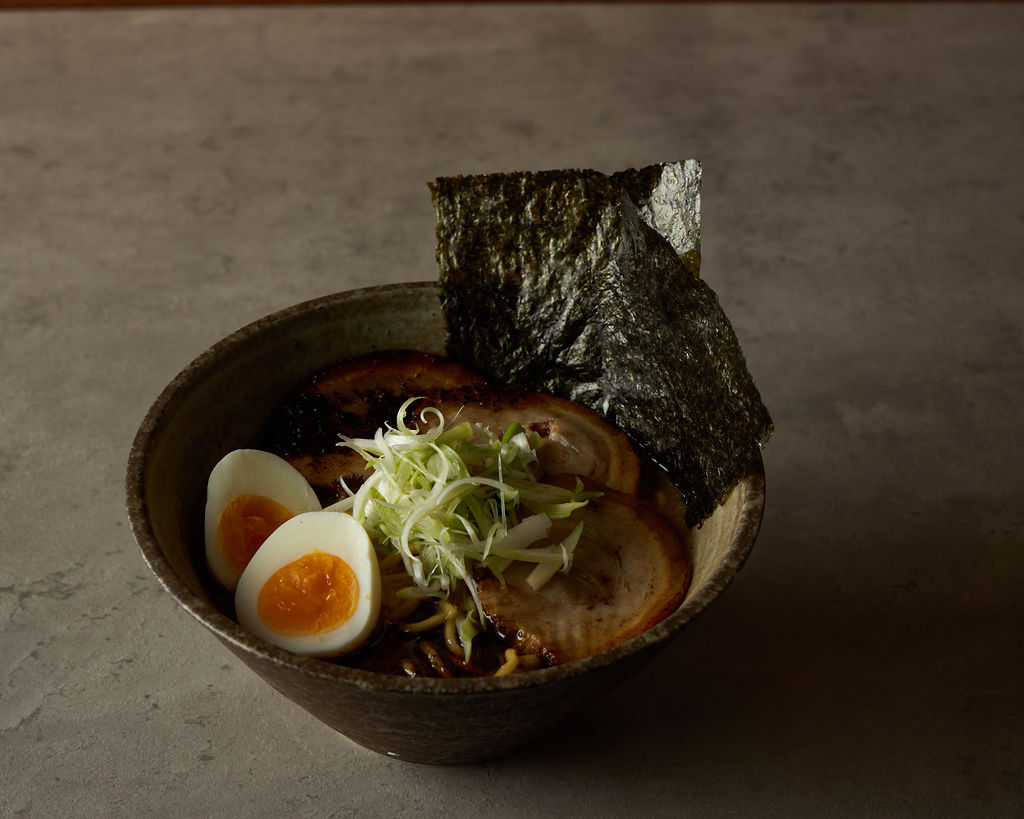 Dark earthenware ramen bowl with shredded leek and chashu pork